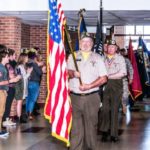 Veterans carrying flags in school ceremony.