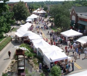 Outdoor street fair with white tents and crowds.
